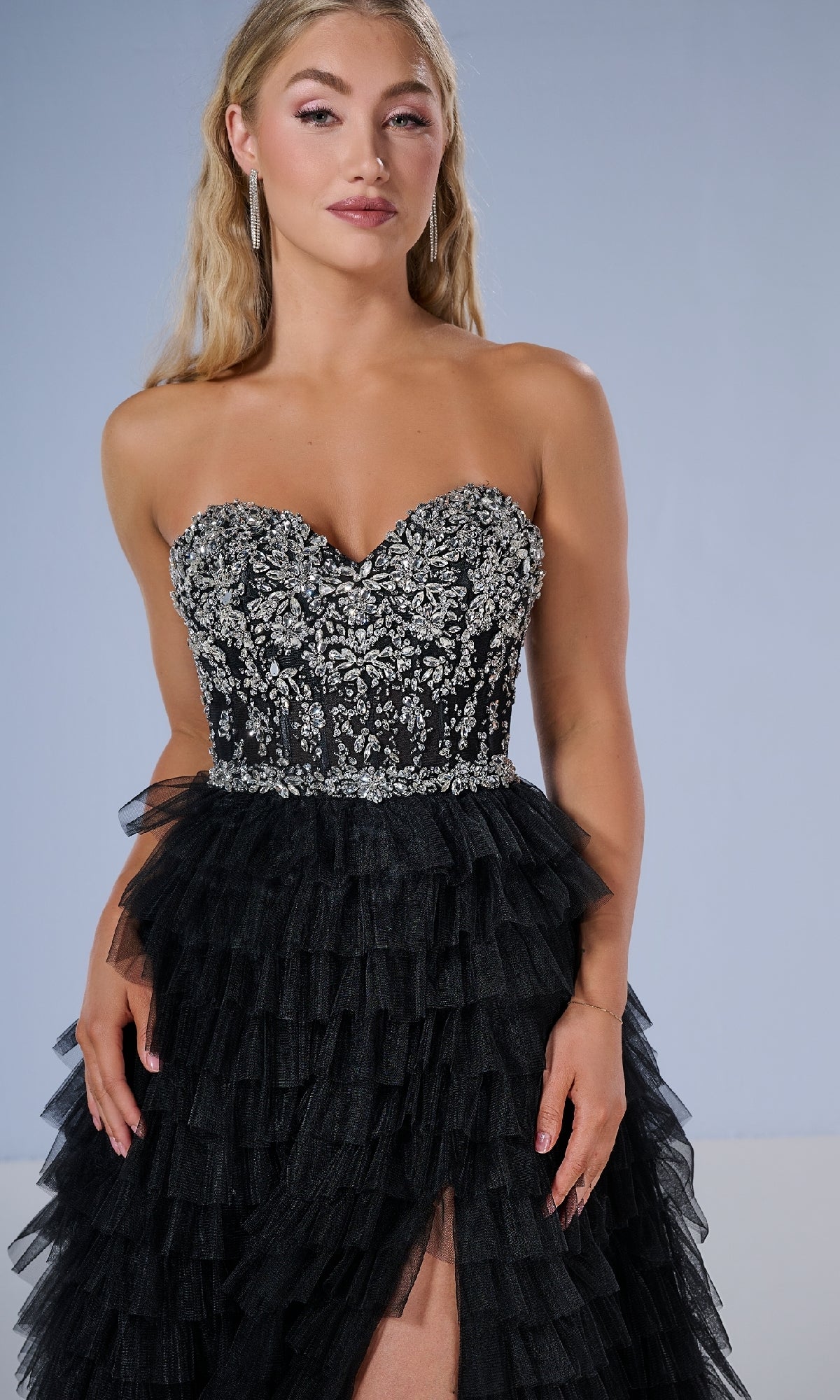 A woman wears the Long Prom Dress: Tiffany 16220, a strapless gown with a beaded sweetheart bodice, silver embroidery, and a tiered ruffle skirt, standing against a plain light background.
